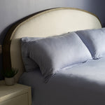 Bedroom with a bed featuring light blue bedding and pillows, a nightstand with a lamp, and a lamp on the wall.