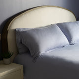 Bedroom with a bed featuring light blue bedding and pillows, a nightstand with a lamp, and a lamp on the wall.