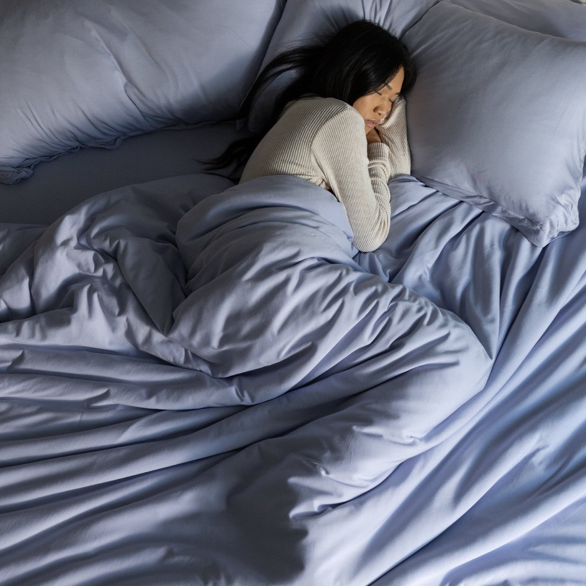 Person lying in bed under a blue comforter with pillows from top down
