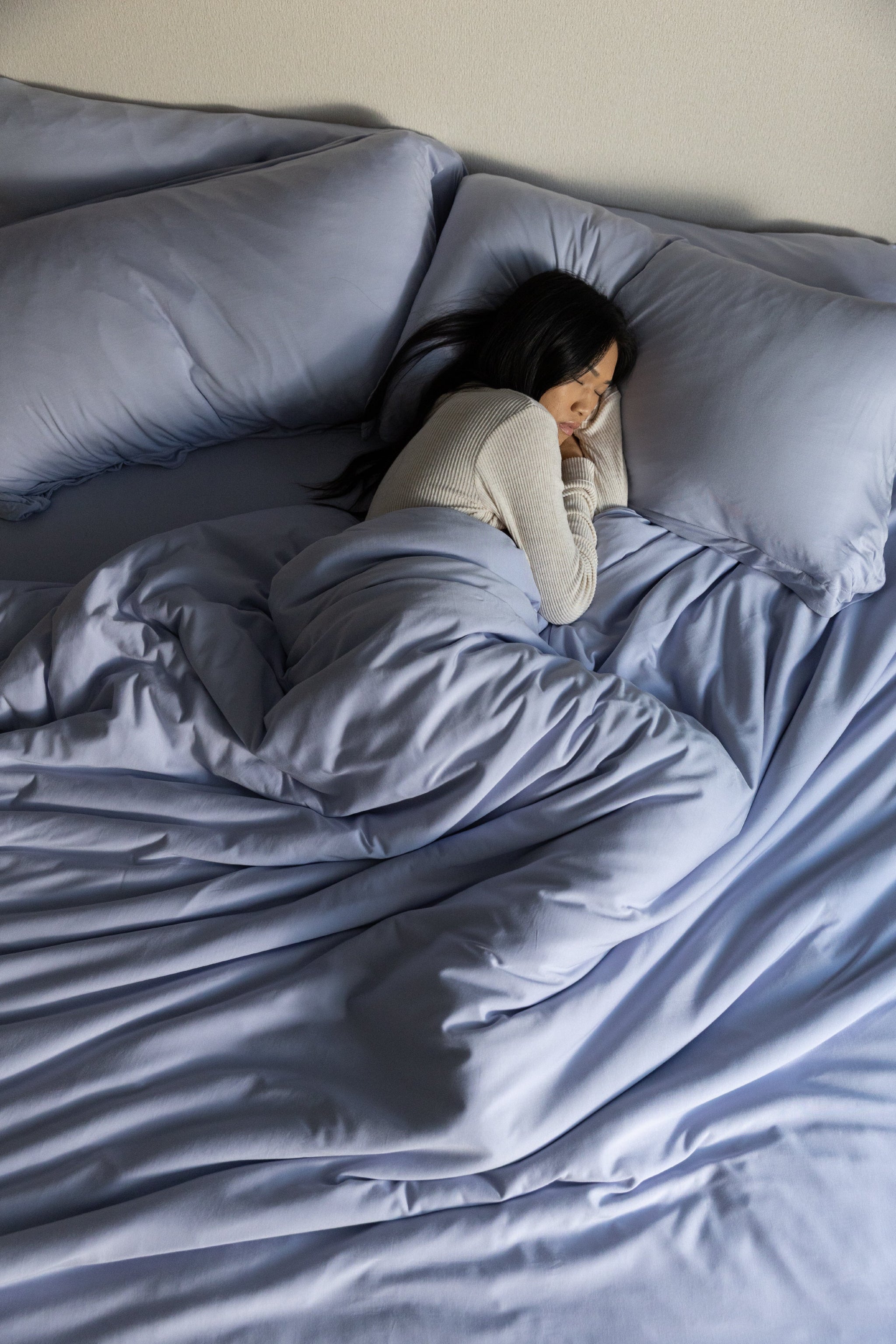Person lying in bed under a blue comforter with pillows from top down