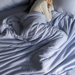 Person lying in bed under a light blue comforter
