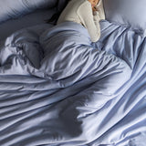 Person lying in bed under a light blue comforter