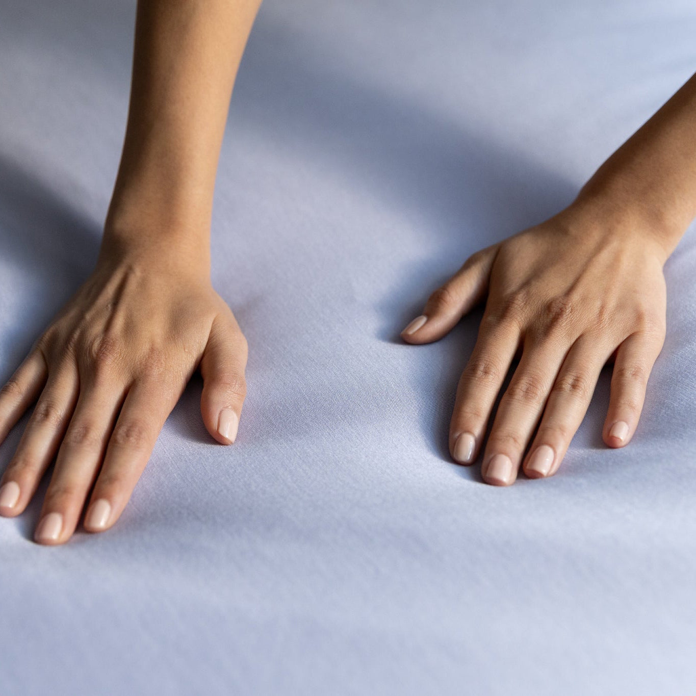 Two hands resting on a light blue jersey knit fabric
