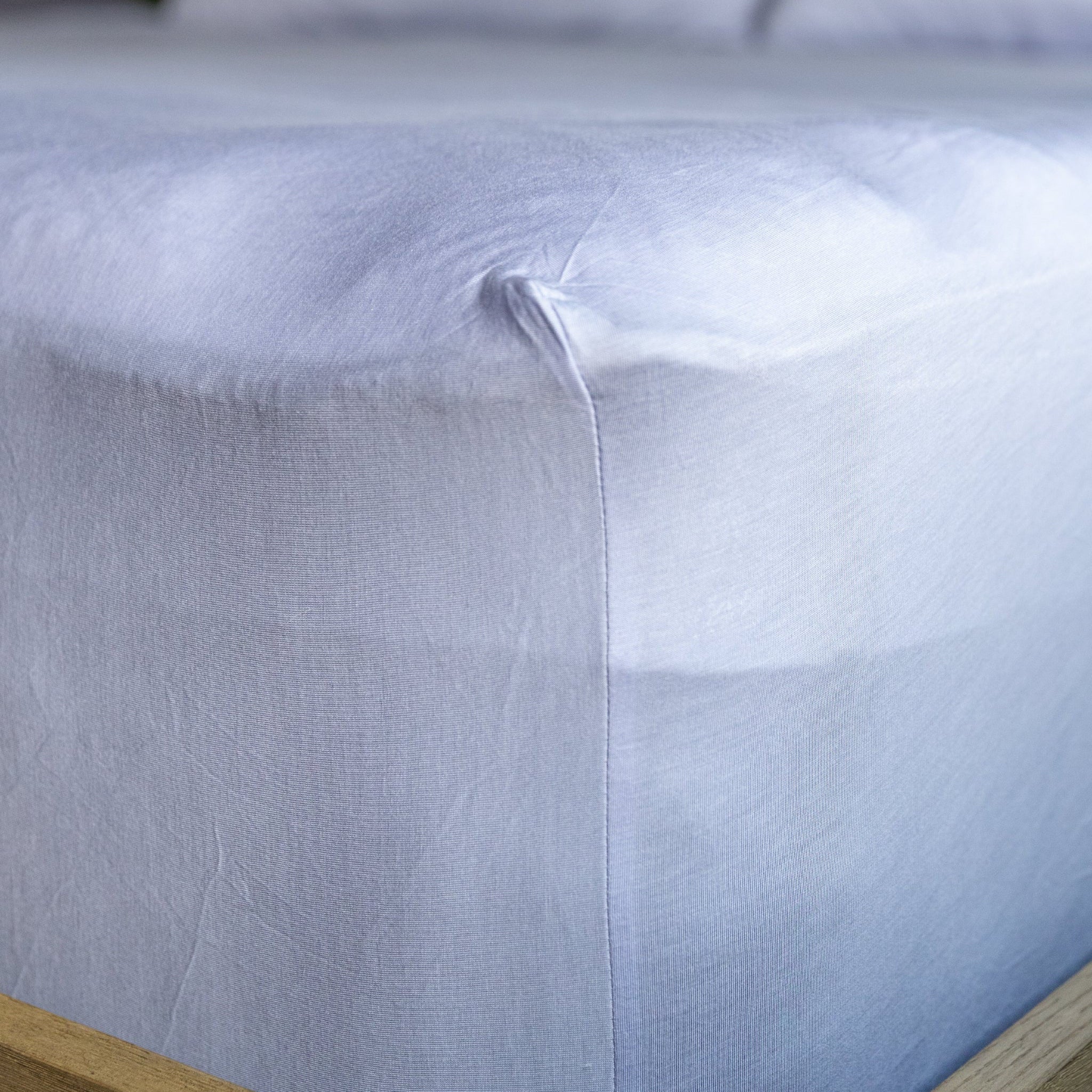 Close-up of a light blue fitted sheet on a bed with wooden frame