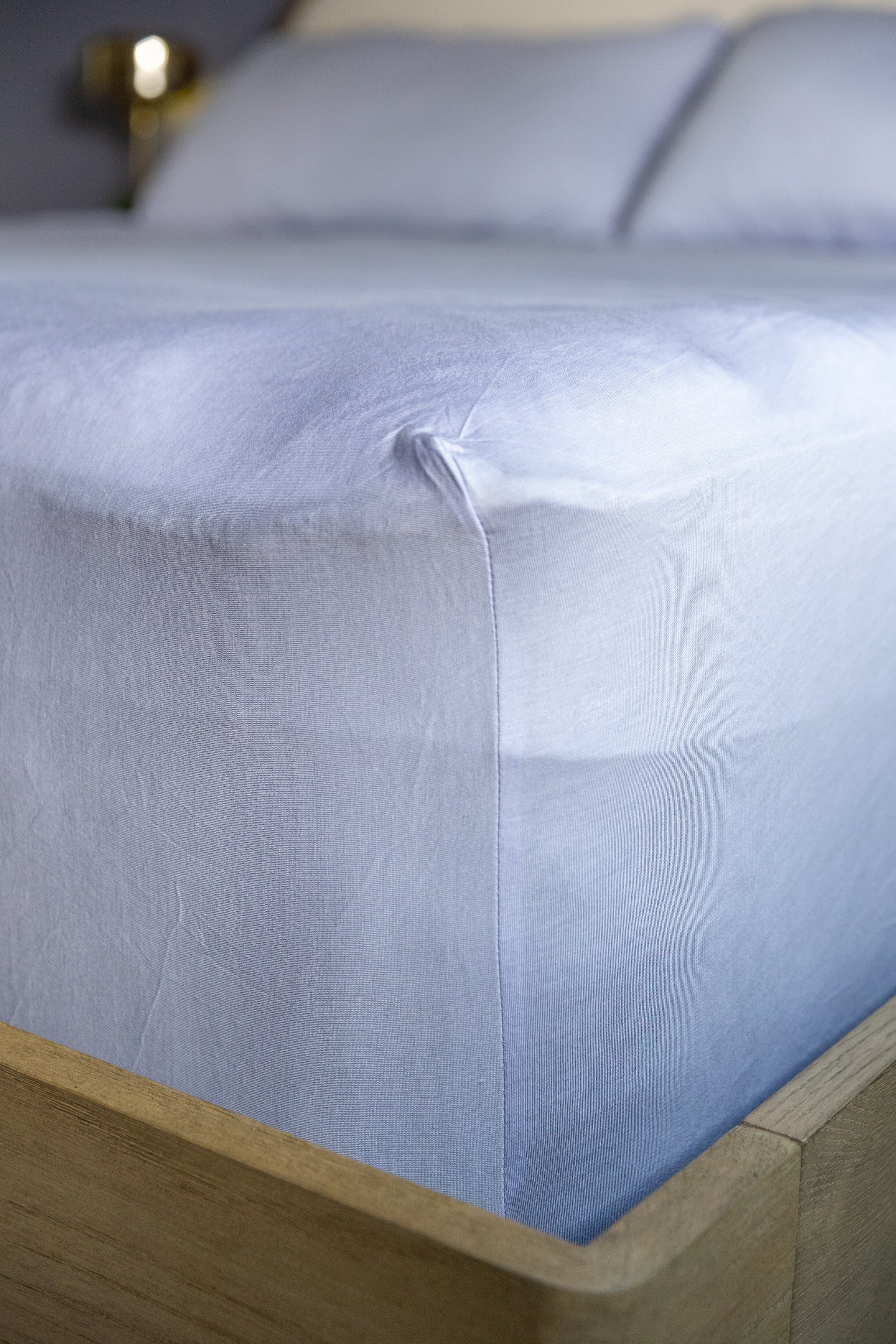 Close-up of a light blue fitted sheet on a bed with wooden frame