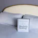 Box of BleuBully Bedding on a bed with light blue bedding and headboard.