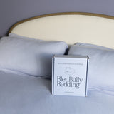 Box of BleuBully Bedding on a bed with light blue bedding and headboard.
