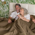 older Couple lying in bed together with a tropical-themed wallpaper.