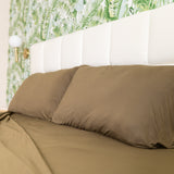 Brown bed sheets on a bed with a white headboard and floral wallpaper.