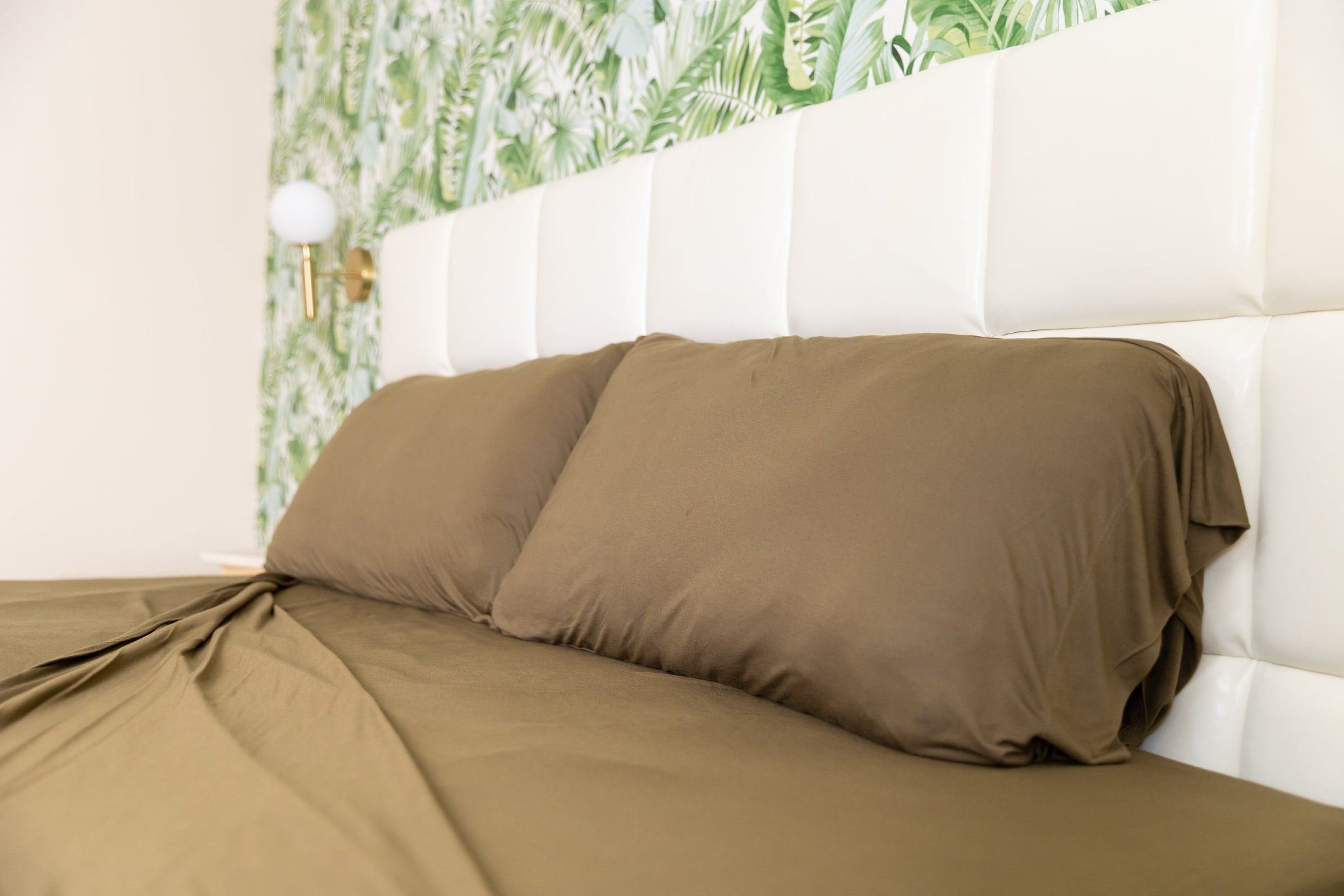 Brown bed sheets on a bed with a white headboard and floral wallpaper.