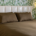 Bed with brown bedding and pillows against a leaf-patterned wall.