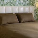 Bed with brown bedding and pillows against a leaf-patterned wall.