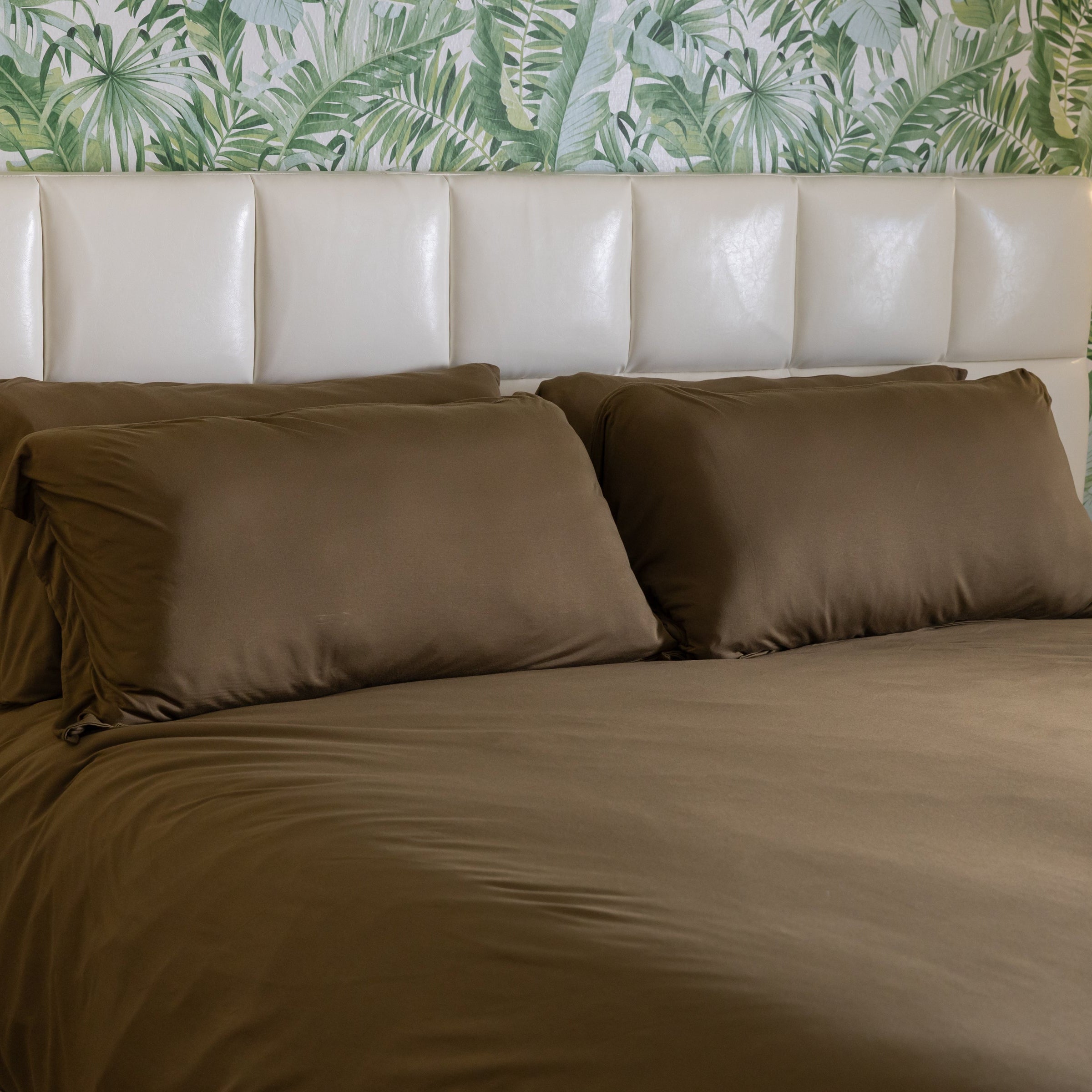 Bed with brown bedding and pillows against a leaf-patterned wall.