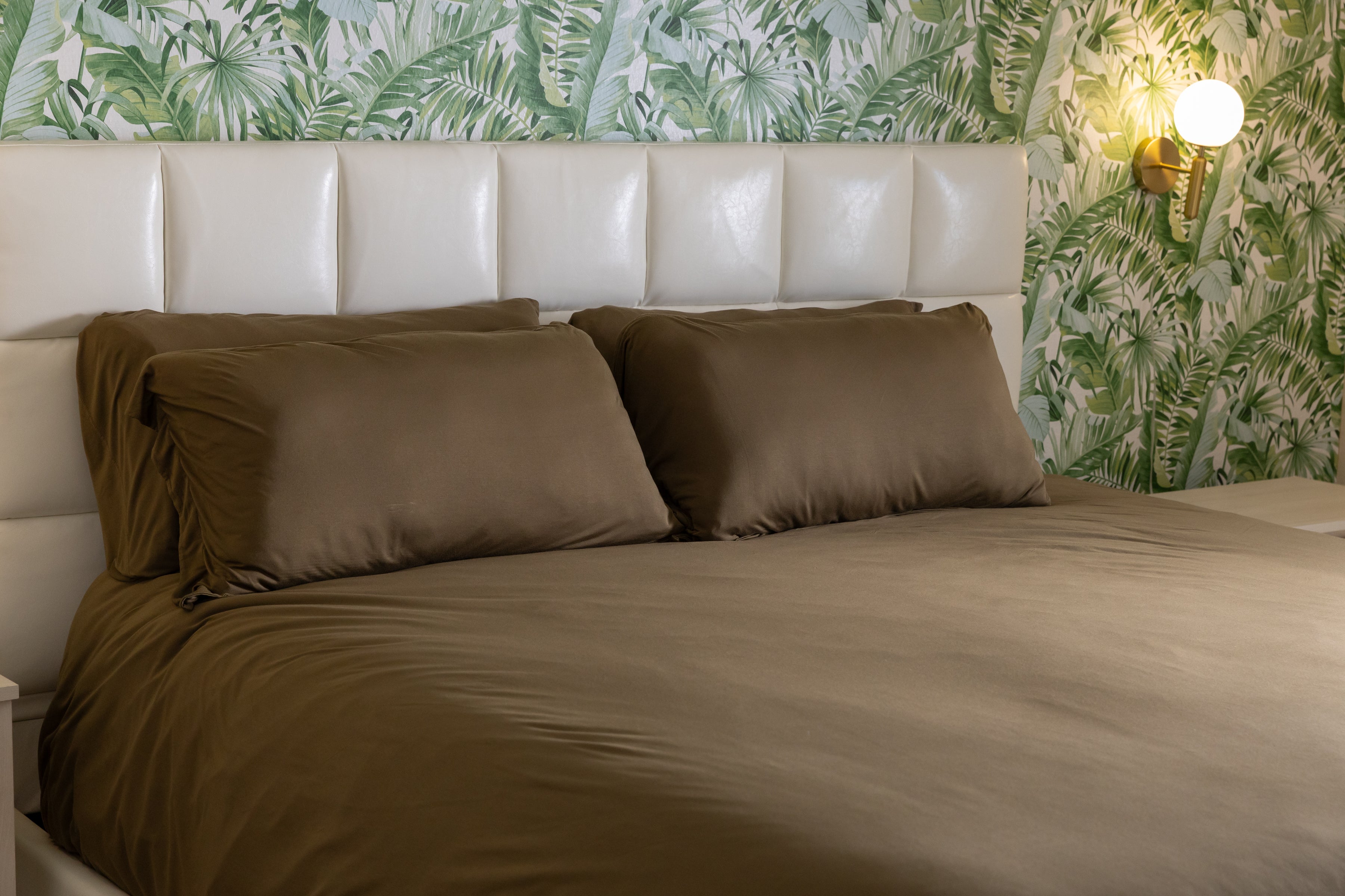 Bed with brown bedding and pillows against a leaf-patterned wall.