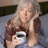 Woman in bed holding a cup of coffee with a neutral background
