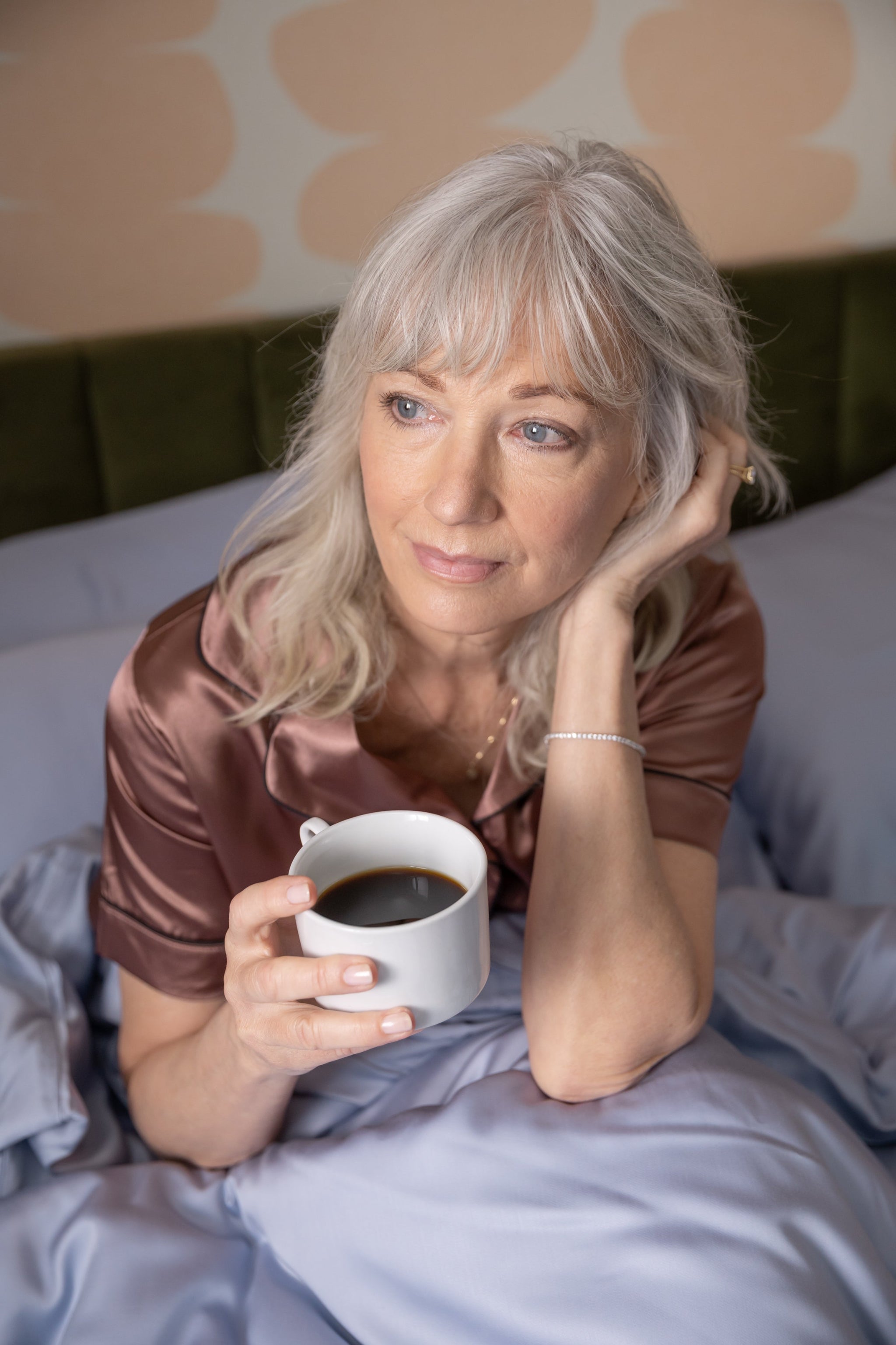 Woman in bed holding a cup of coffee with a neutral background