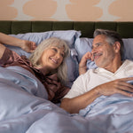 Couple lying in bed together, smiling and embracing on dream blue sateen sheets