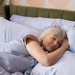 Woman sleeping peacefully in bed with green headboard and light blue bedding.